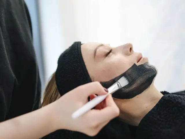 Косметологиня пензлем наносить чорну вуглецеву маску на обличчя жінки